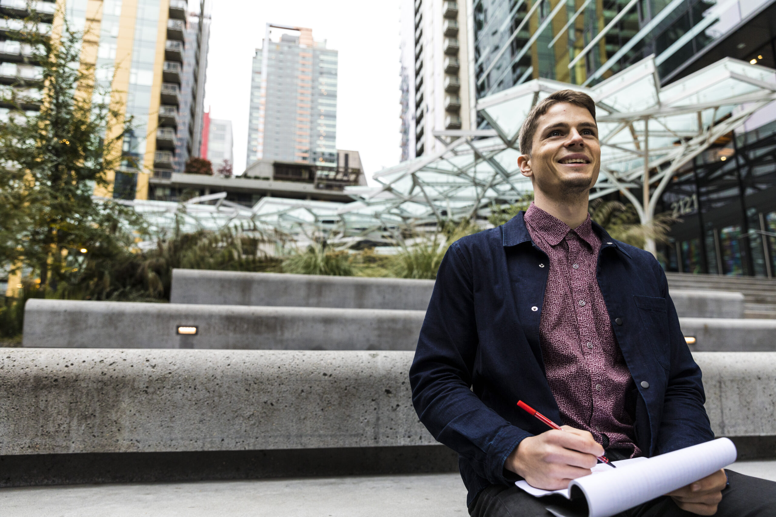 a grad student sits outside a building in downtown Seattle writing in a notebook