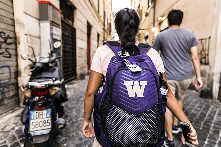 view from behind a person walking through a european street while wearing a university of washington backpack 