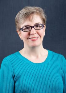 Mary Herbert smiling with short brown hair black rim glasses facing the camera 